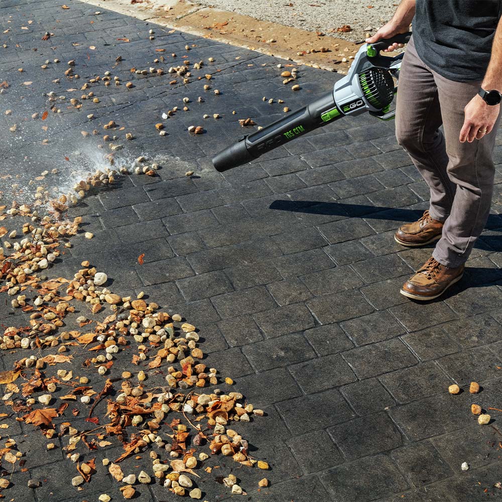 EGO handheld battery blower clearing fallen leaves from a stone path